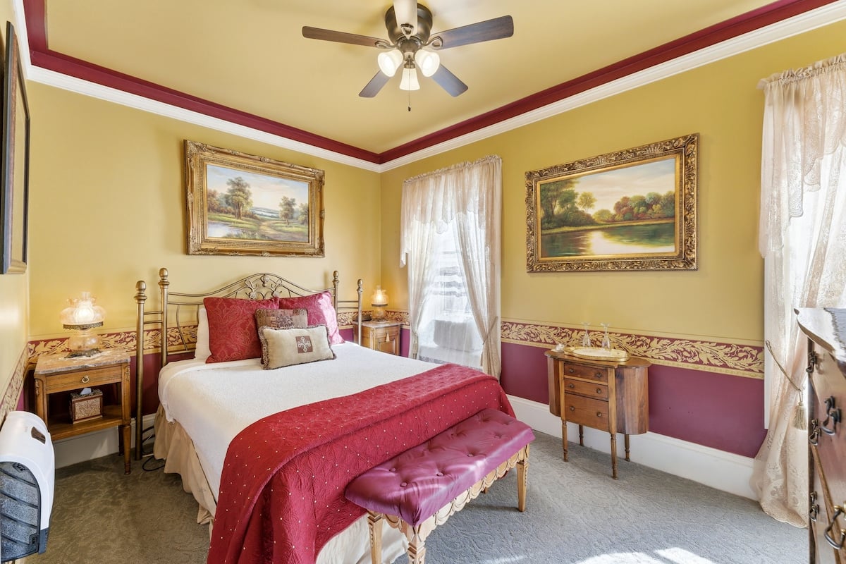 A bedroom with a bed, a bench, a nightstand, a dresser, and a ceiling fan.