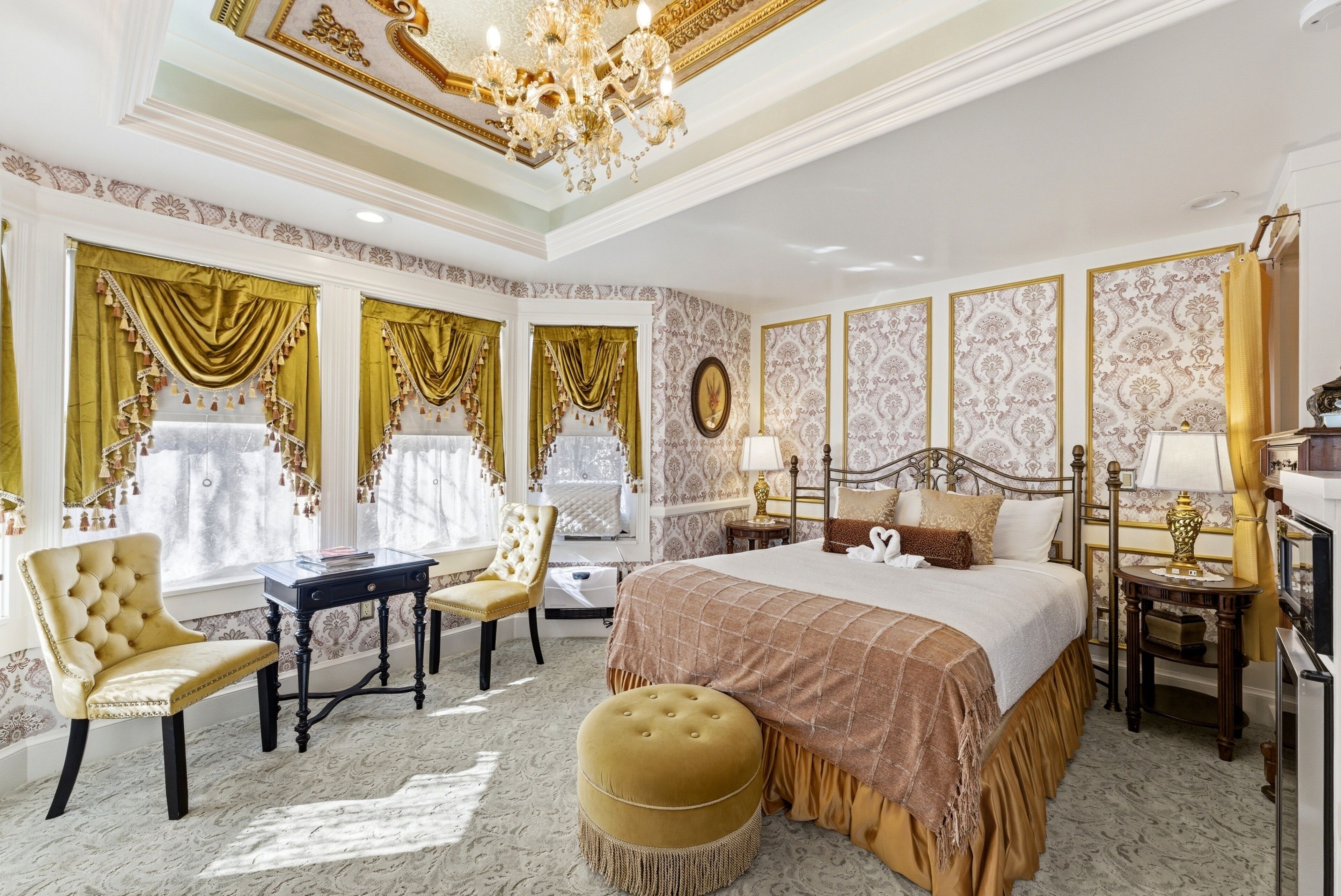 A luxurious bedroom with a large bed, ornate curtains, a chandelier, and a classic design.