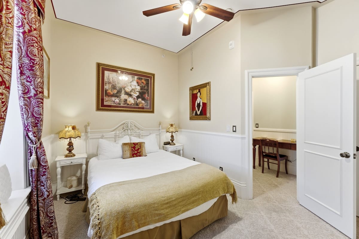 A bedroom with a bed, nightstands, a ceiling fan, a chair, and a door.