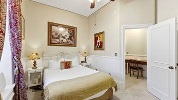 A bedroom with a bed, nightstands, a ceiling fan, a chair, and a door.