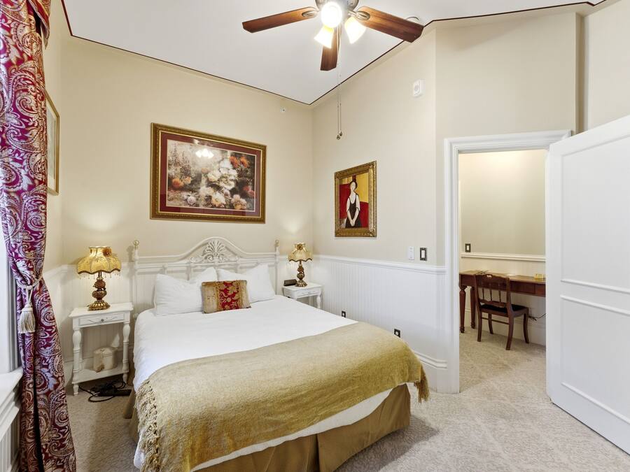 A bedroom with a bed, nightstands, a ceiling fan, a chair, and a door.