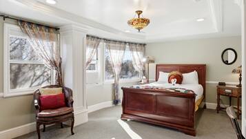 Une chambre à coucher avec un grand lit, une chaise, une table de chevet, un miroir et une fenêtre avec des rideaux.