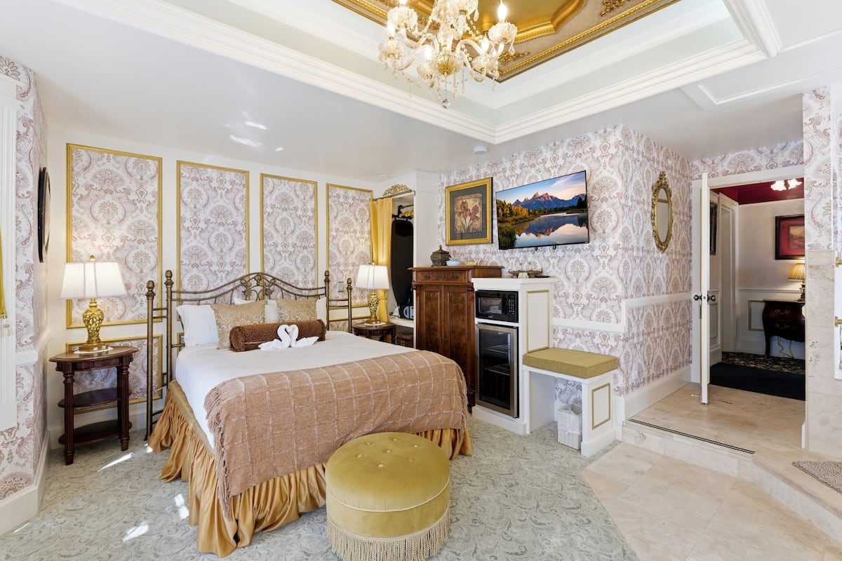 A luxurious bedroom with a large bed, a television, a fireplace, and a view of the outdoors.