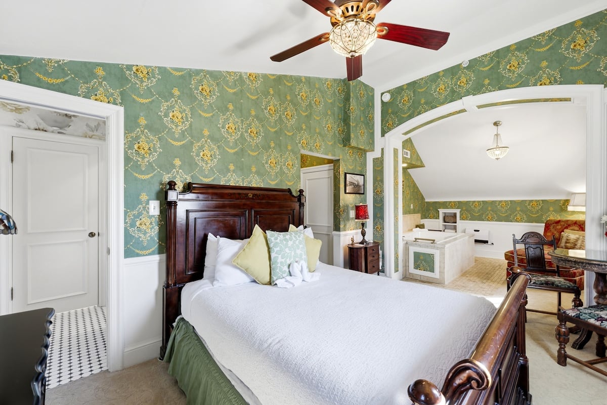 A bedroom with a large bed, a ceiling fan, a desk, and a chair.