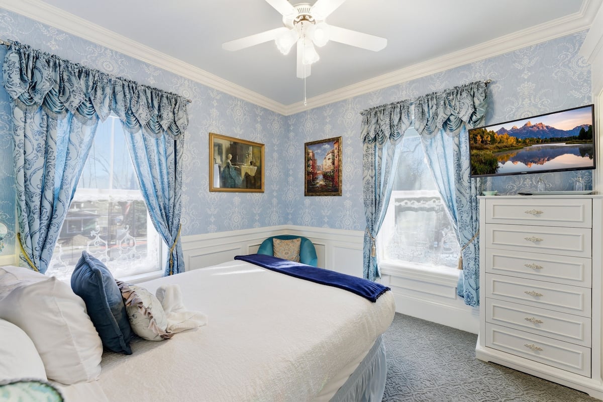 A bedroom with a bed, a dresser, a television, and two paintings.