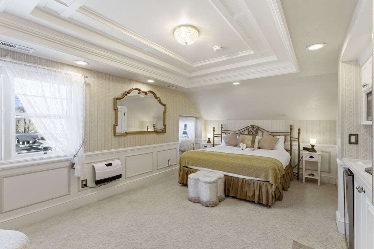 A bedroom with a large bed, a nightstand, a dresser, a mirror, and a window with curtains.