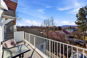 A balcony with a glass table and chairs, a white railing, and a view of a residential area with houses and trees. - Heber Senator Bed and Breakfast (Heber City)