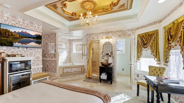 A luxurious bedroom with a large bed, a television, a chandelier, a bathroom with a bathtub, and a dining area with a table and chairs. - Heber Senator Bed and Breakfast (Heber City)