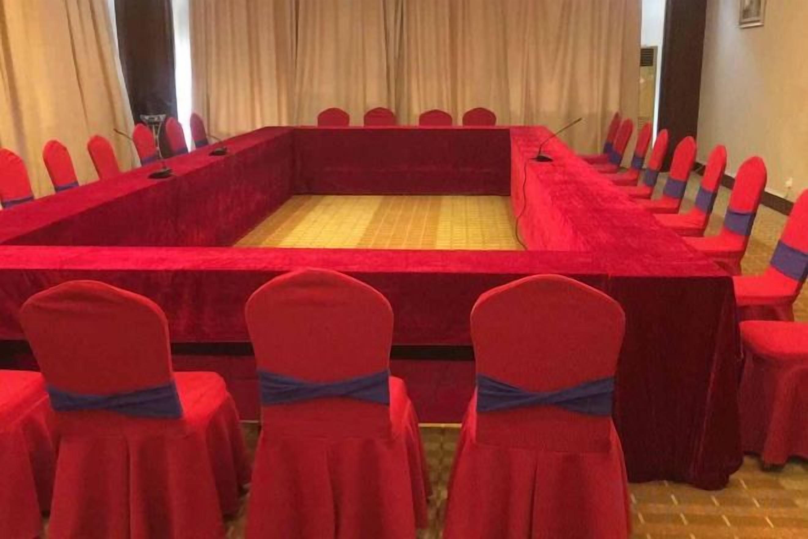 A conference room with a long rectangular table and red chairs with blue sashes.