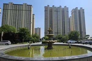 Una fuente circular con cascadas escalonadas rodeada de una zona pavimentada, con edificios residenciales altos al fondo.