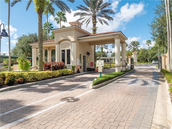 A gated entrance with a covered walkway, palm trees, and a clear sky.