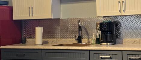 A kitchen with grey cabinets, a red refrigerator, a coffee maker, and a sink.