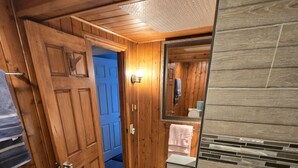 Ein Badezimmer mit Holzwänden, einem Spiegel, einem Handtuchhalter und einer Duschkabine.
