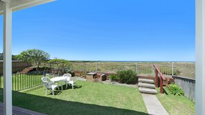 A patio with a table and chairs, a brick barbecue, and a view of the ocean. - Oceanside - Pet Friendly Beachside Accommodation (AVOCA BEACH)