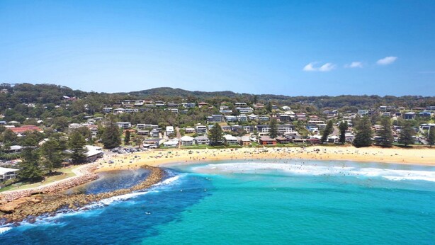 A coastal town with a beach, houses, and a rocky shoreline.