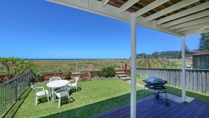 A covered patio with a view of the ocean, a barbecue grill, and a small table with chairs.