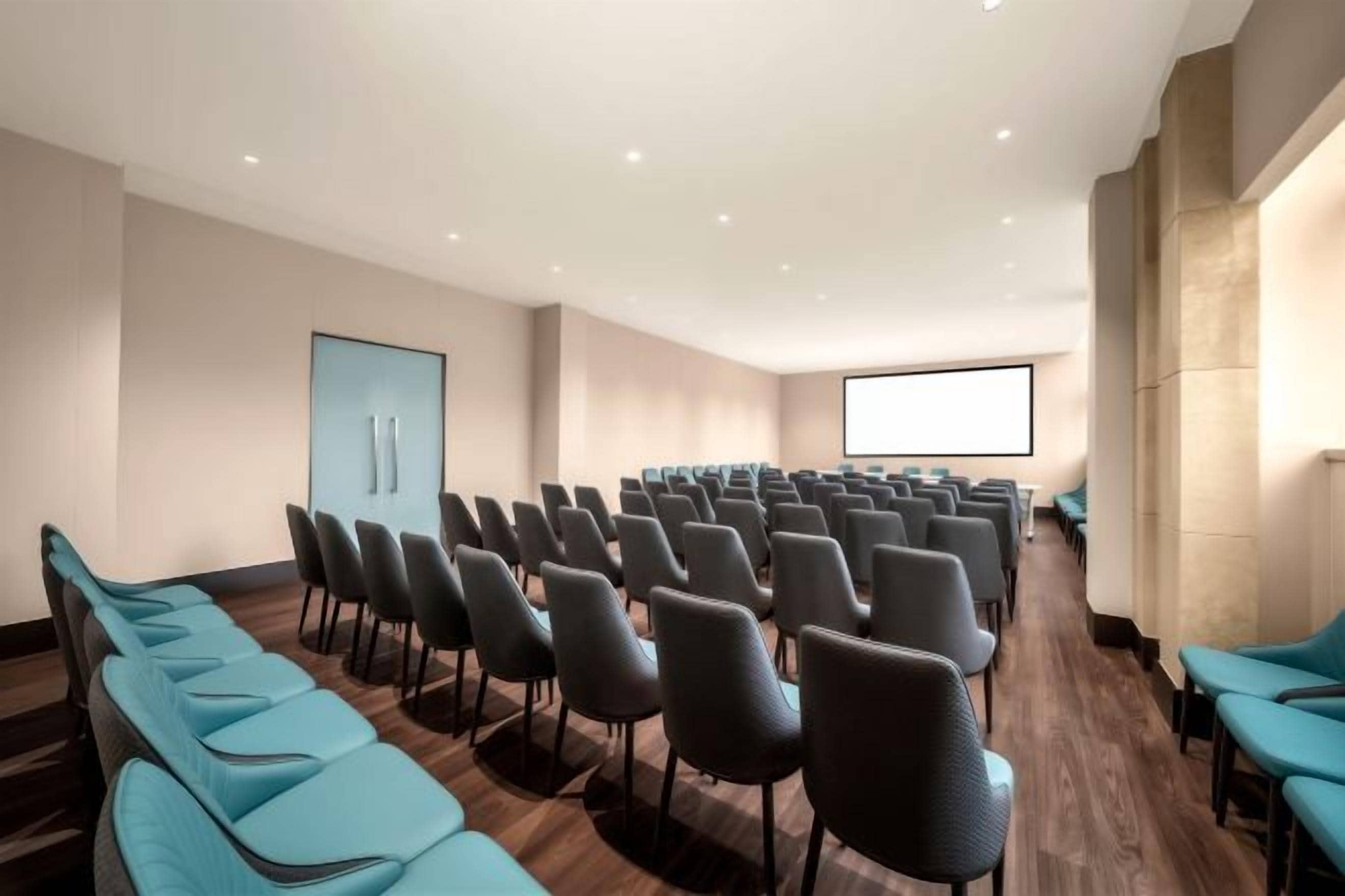 A conference room with rows of chairs, a large screen, and a wooden floor.