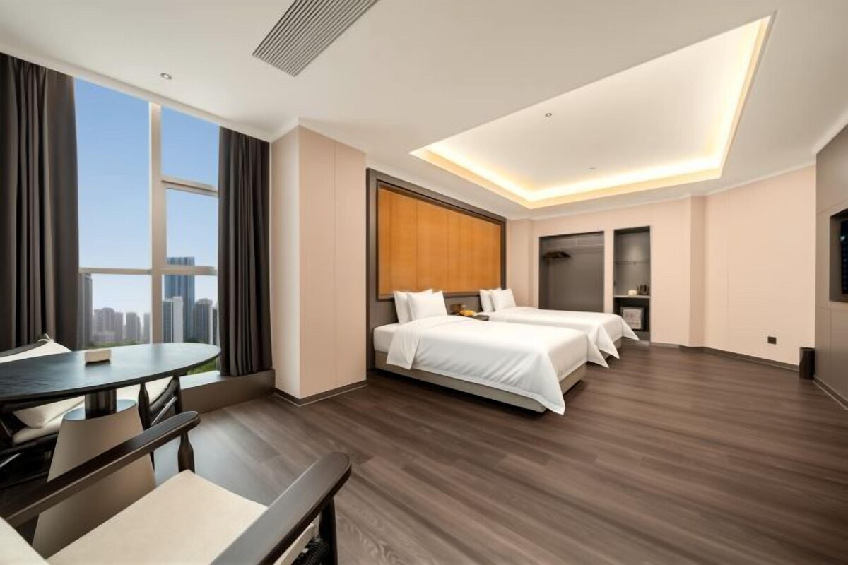 A hotel room with a bed, a desk, a chair, a window with a city view, and a modern ceiling design.