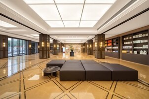 Un vestíbulo amplio con una zona de estar central, una recepción y un ventanal con vistas al exterior.