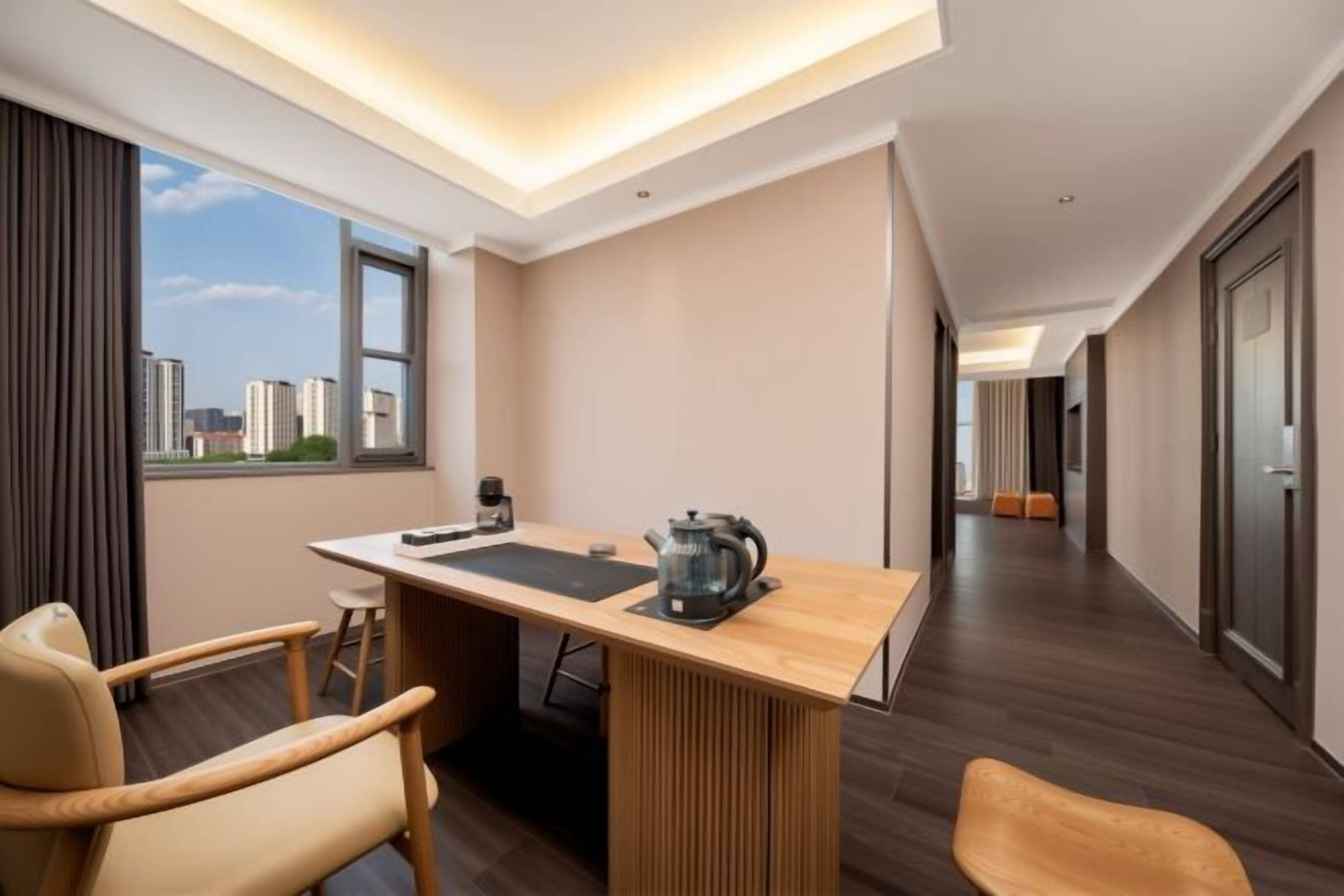 Une chambre d’hôtel moderne avec un bureau en bois, deux chaises, une machine à café et une vue sur la ville.