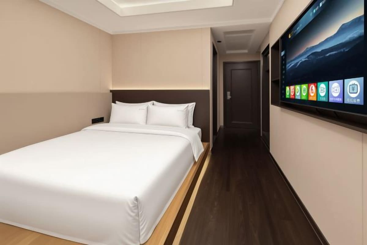 Una habitación de hotel con una cama, un televisor montado en la pared y un pasillo que conduce a otra habitación.