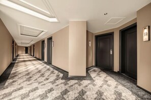 Un pasillo de hotel con alfombra estampada, puertas oscuras e iluminación empotrada.