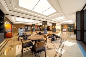 Un amplio hall de hotel con varias zonas de estar, una recepción y una gran lámpara de araña.