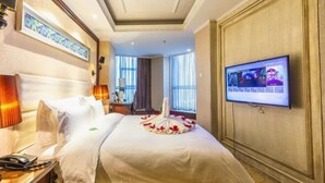 Hotellihuone, jossa on sänky, televisio, kirjoituspöytä puhelimineen ja ikkuna, jossa on verhot.