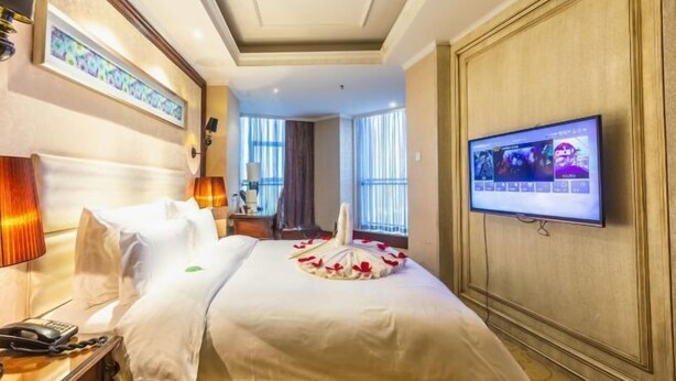 Quarto de hotel com cama, televisão, escrivaninha com telefone e janela com cortinas.