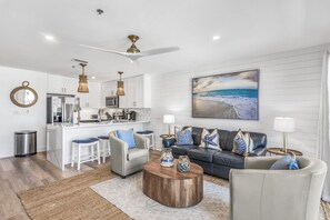 A modern living room with a sofa, coffee table, and a dining area with bar stools.