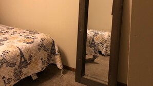 Un dormitorio con una cama cubierta por un edredón estampado con motivos florales, un espejo con marco de madera apoyado contra la pared, y suelo alfombrado.