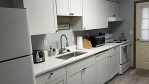Una cocina con armarios blancos, un lavamanos de acero inoxidable, un microondas y una estufa.