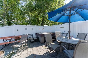 Un patio exterior con una mesa, sillas, una sombrilla azul y un jacuzzi.