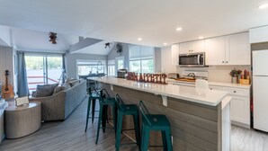 Una cocina moderna con armarios blancos, una isla grande, taburetes de bar y una guitarra sobre una mesita.