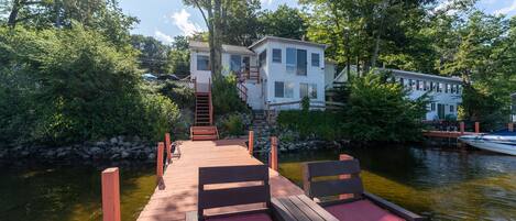 A wooden dock with benches, a stone wall, and a house with a staircase leading to a second floor.