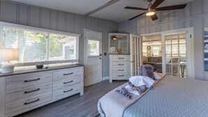 Un dormitorio con cama, cómoda, ventilador de techo y ventana con persianas.