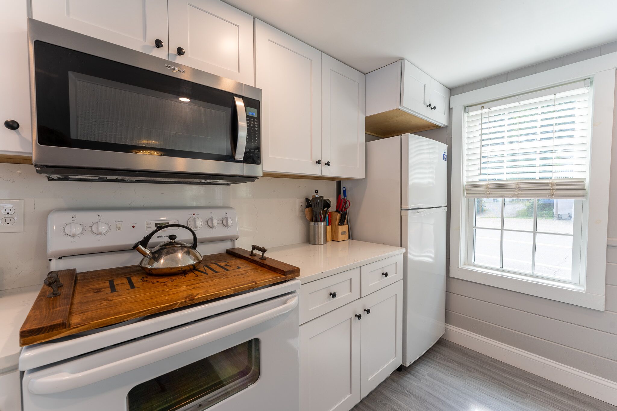 A kitchen with white cabinets, a stainless steel microwave, a white stove, and a white refrigerator.
