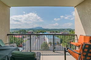 Enjoy the expansive view from this balcony, featuring a sofa and chair, overlooking the parking lot and surrounding landscape.