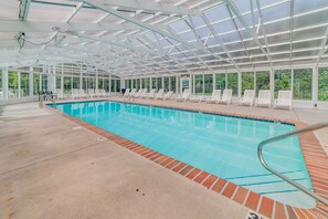 An indoor swimming pool with clear glass ceilings, white lounge chairs, and a brick border around the pool. - Bear's Den • Walk to attractions • Mountain View Condo • Virtual Checkin (Pigeon Forge)