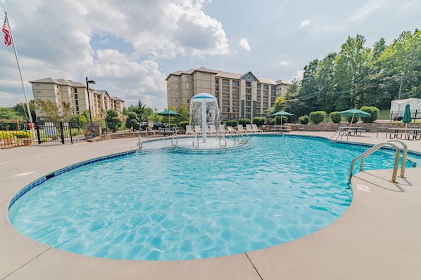 Relax by the circular pool surrounded by lounge chairs and umbrellas, with a central fountain feature.