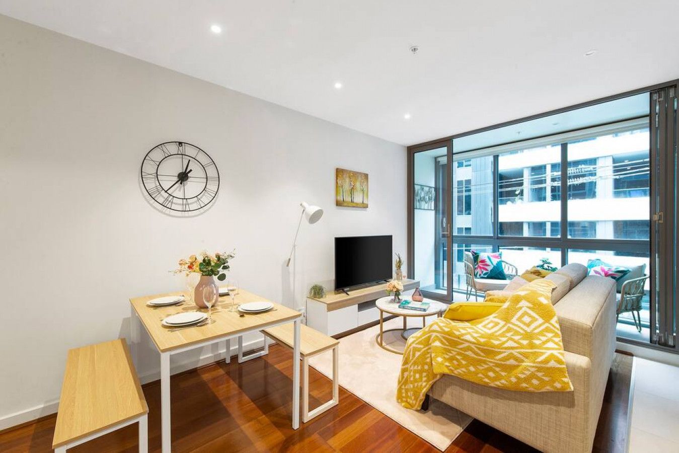 A modern living room with a sofa, a dining table, a TV, and a large window.