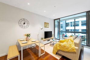 A modern living room with a sofa, a dining table, a TV, and a large window.