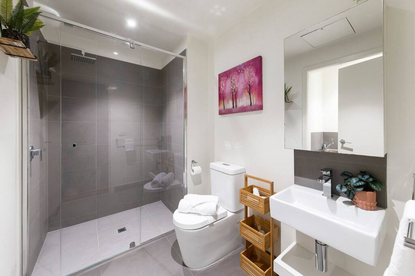 A modern bathroom with a glass-enclosed shower, a white toilet, a sink with a mirror, and a wooden storage unit.