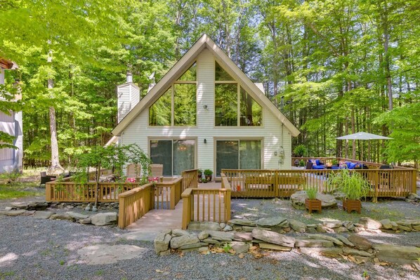 A cabin with a triangular roof, large windows, and a deck with seating.