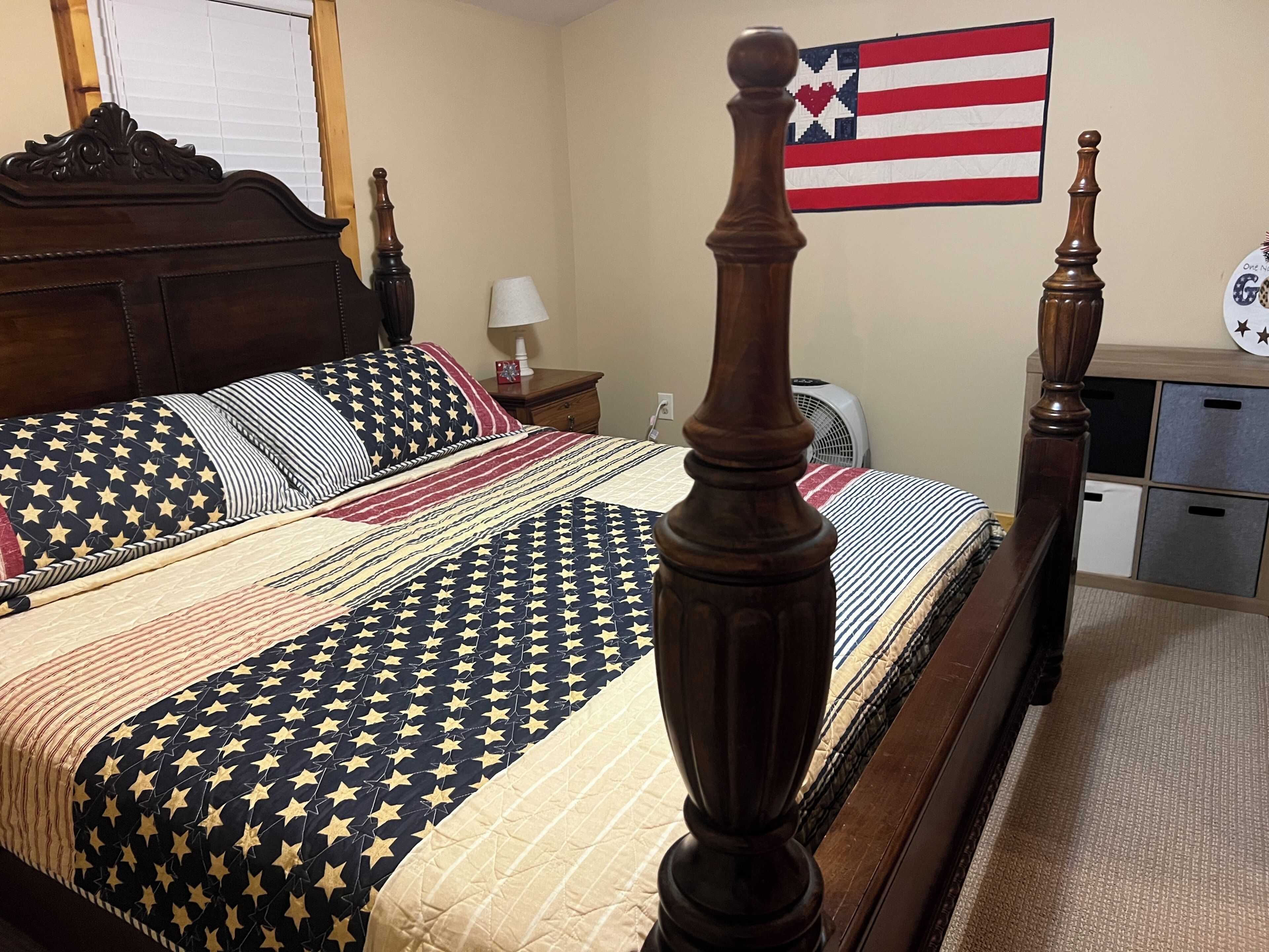 Un dormitorio con una cama que lleva un edredón estampado con motivos de estrellas, un cabecero de madera y una mesita de noche con una lámpara.