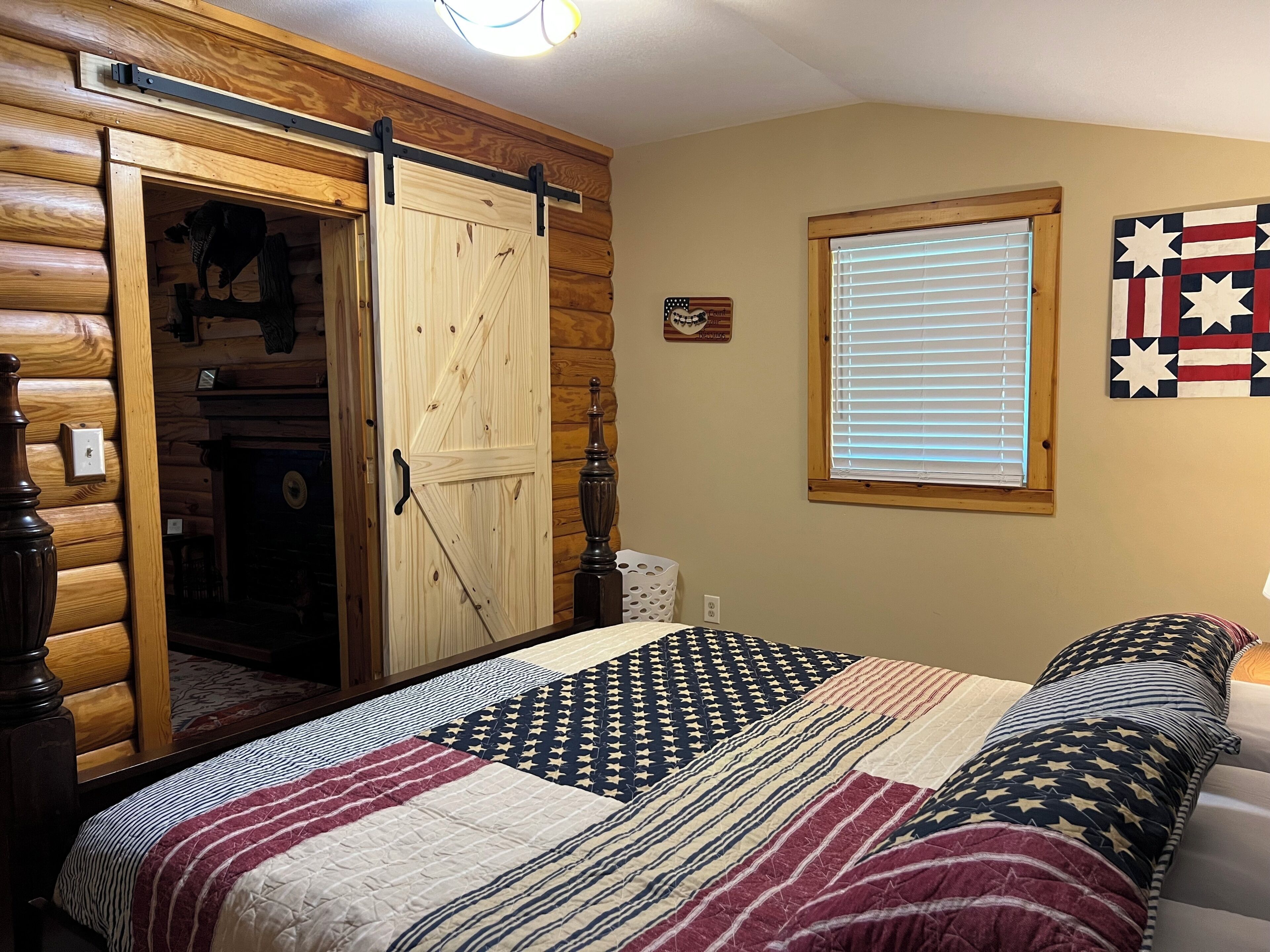Un dormitorio con puerta de madera, ventana con persianas y cama con colcha estampada.