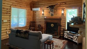 Ein Blockhaus-Interieur mit Kamin, Holzwänden, einer Couch, einem Fernseher und einem Deckenventilator.