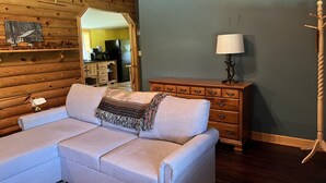 Ein gemütliches Wohnzimmer mit einer Couch, Holzwänden, einer Kommode und einer Lampe.