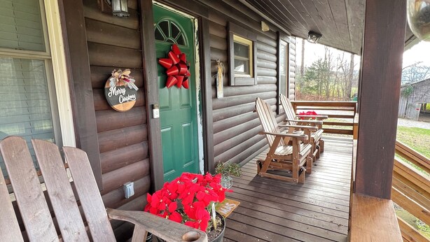 Eine Holzveranda mit einer grünen Tür, roten Schleifchen und einem Weihnachtsgesteck. Holzstühle und eine Bank stehen auf der Veranda.