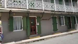 Un bâtiment à deux étages doté d’un balcon, de volets verts et d’une enseigne indiquant que l’établissement est ouvert.